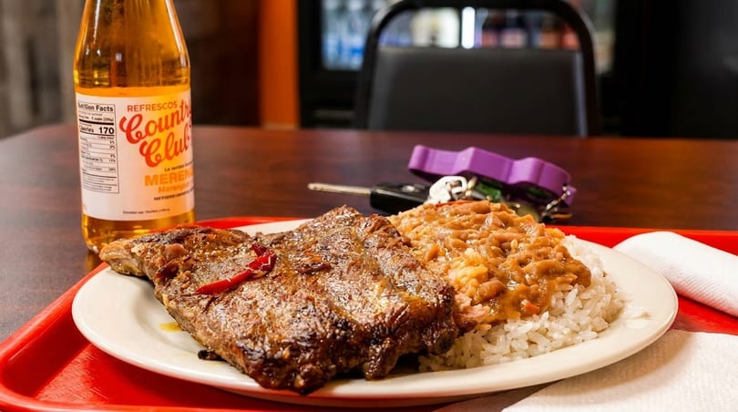 Grilled steak with rice and beans, a Country Club soda, and keys on a red tray.