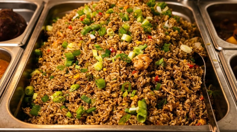 Close-up of a large metal tray filled with shrimp fried rice, garnished with green onions.